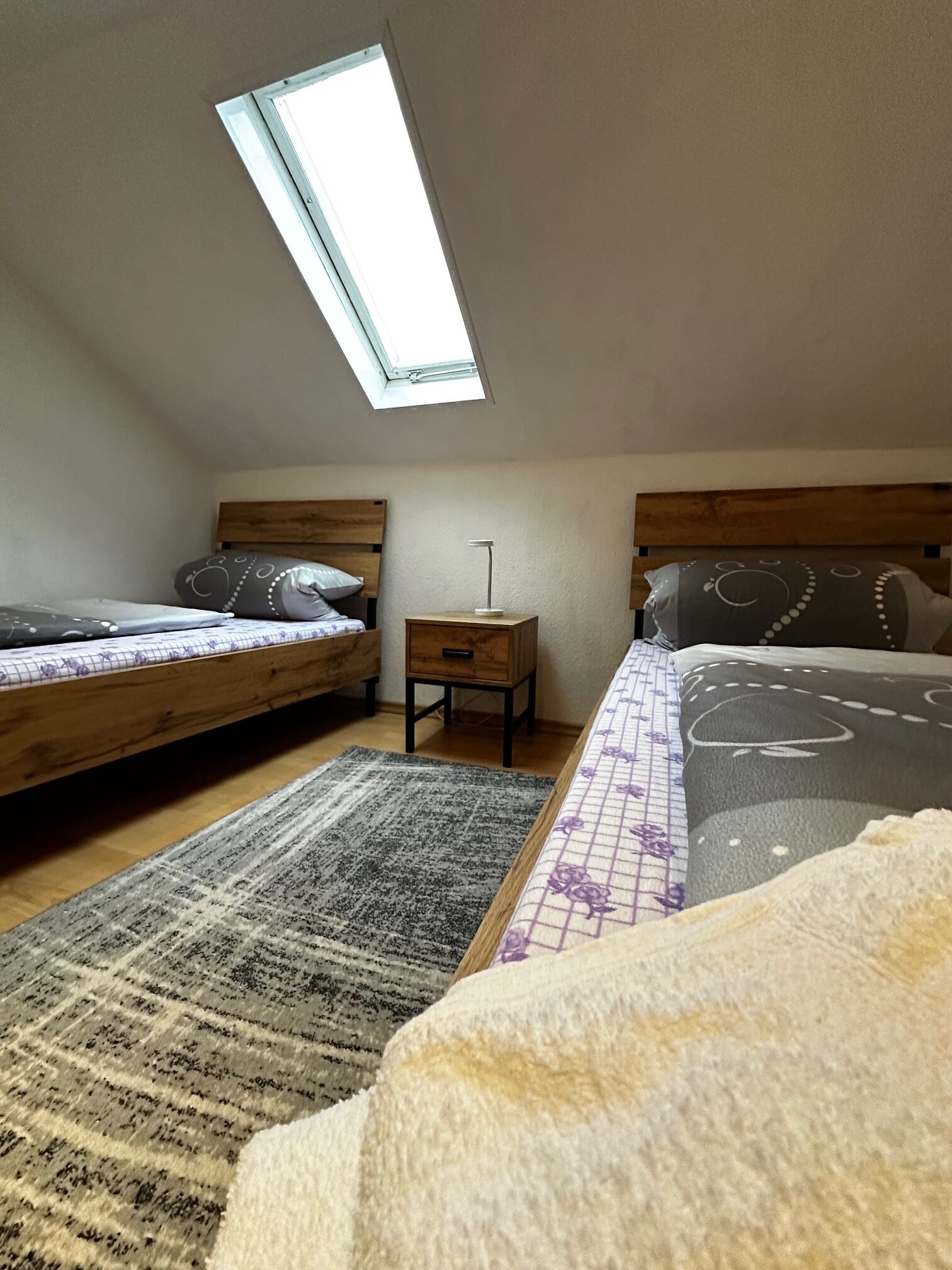 Zwei Einzelbetten in einem Schlafzimmer mit einem Dachfenster und einem Nachttisch.