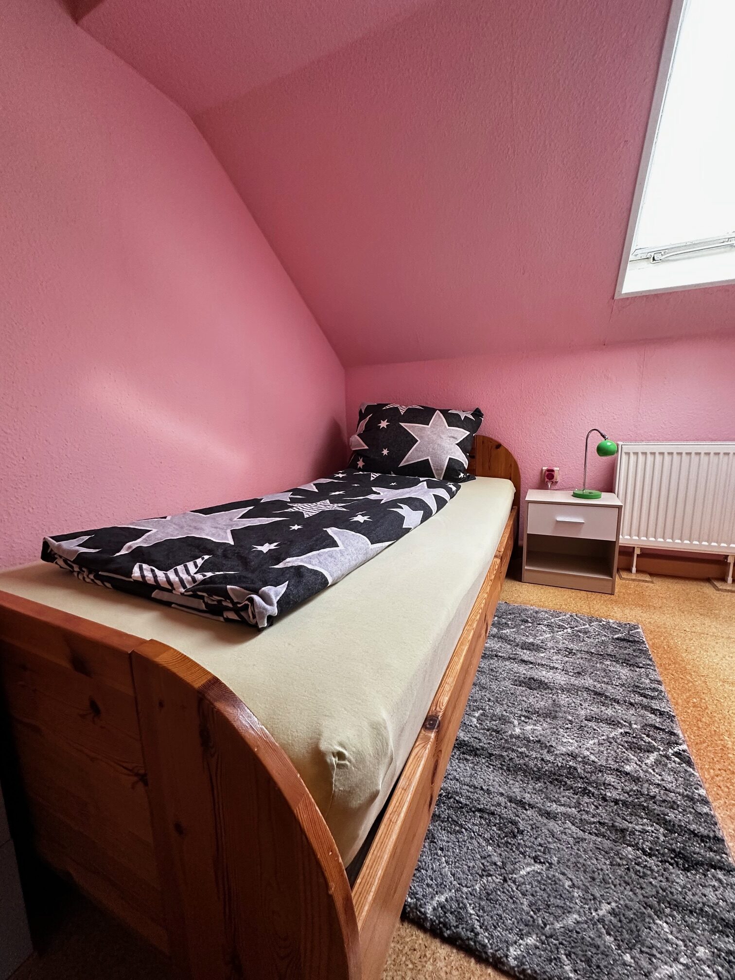Einzelbett mit schwarzer Bettwäsche mit weißen Sternen in einem rosa Zimmer.